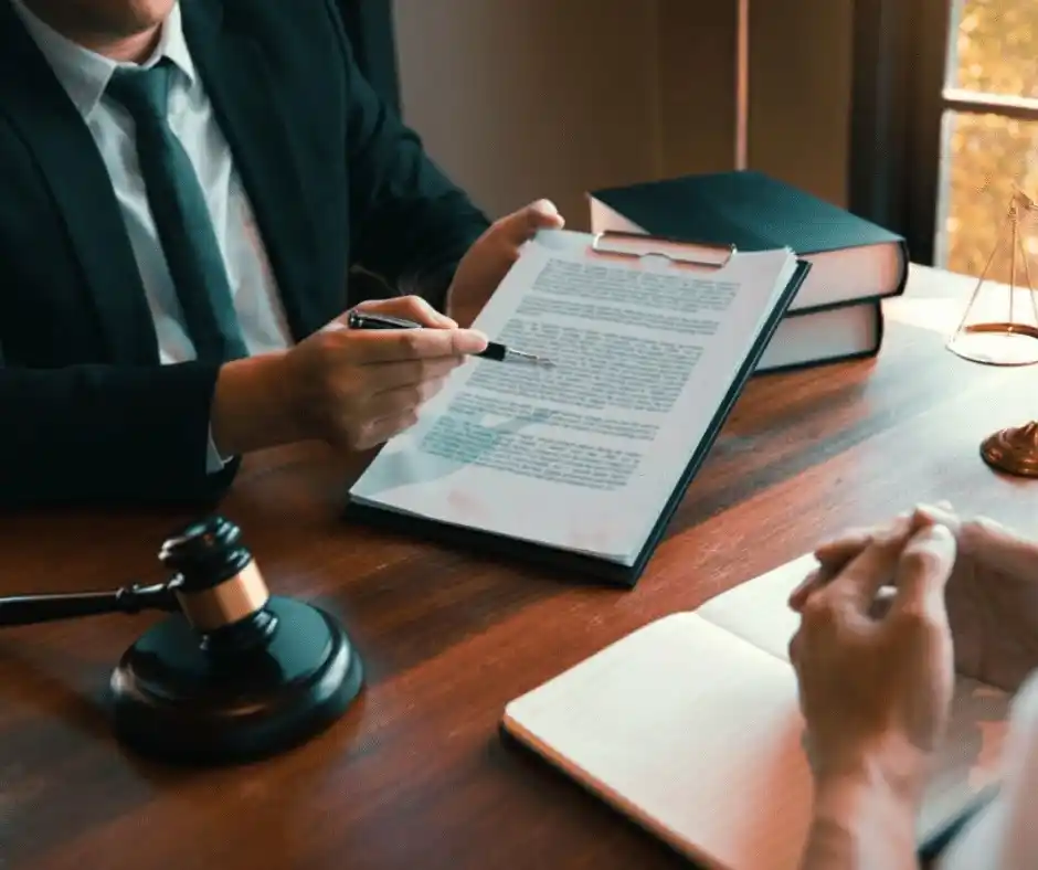  A lawyer in a suit discusses a legal document with a client at a desk, with a gavel, legal books, and notes present, symbolizing employment law consultations. This image represents discussions about double time vs. overtime pay, double time pay in California, and California double time laws, highlighting workers' rights and fair compensation.