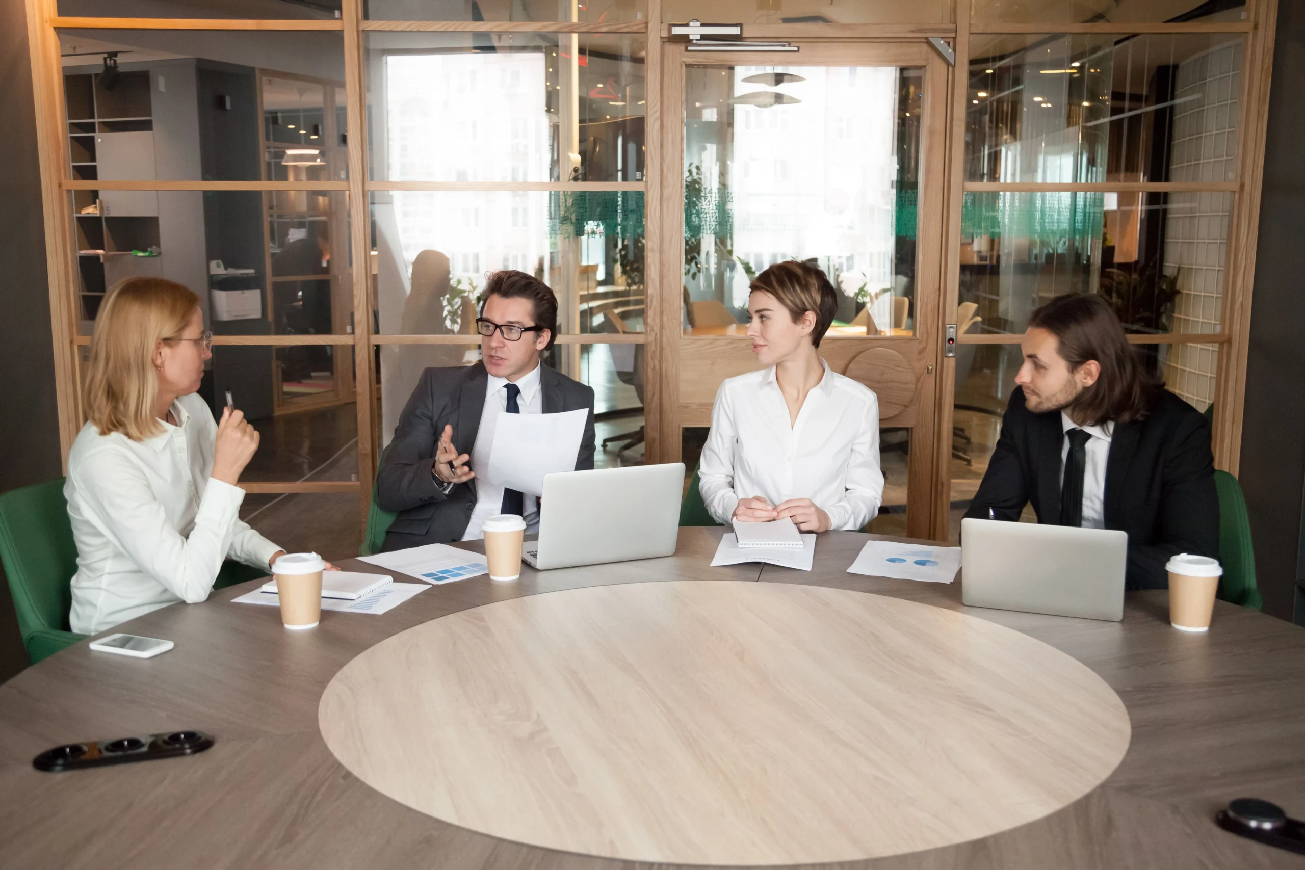 Business professionals collaborate at a table with laptops, discussing strategies for class action lawsuits against corporations