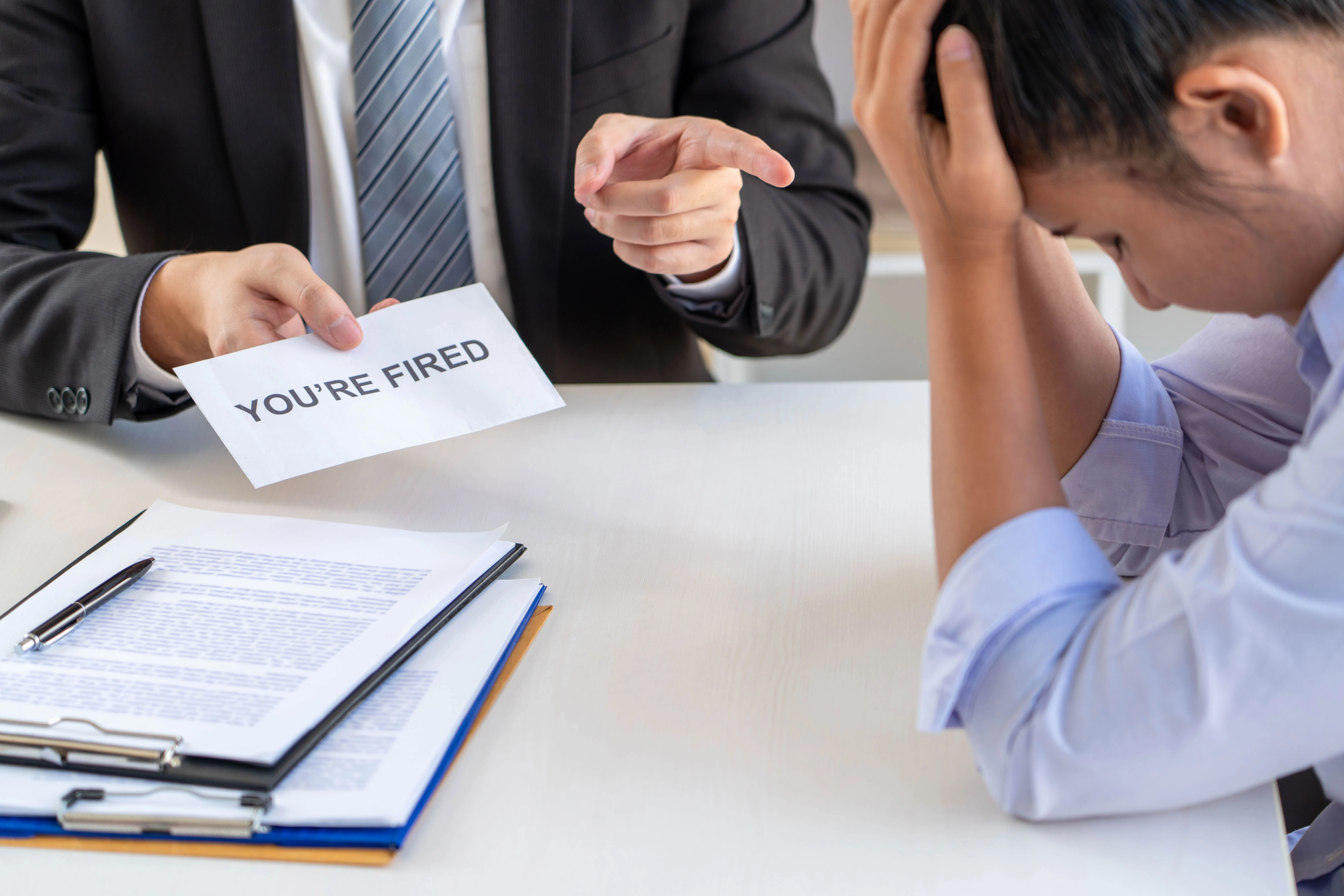 A man and woman are seated at a table, a "You're Fired" sign present, indicating a situation of wrongful termination.